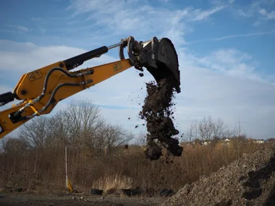 Mini excavator arm dumping soil from its bucket under a blue sky