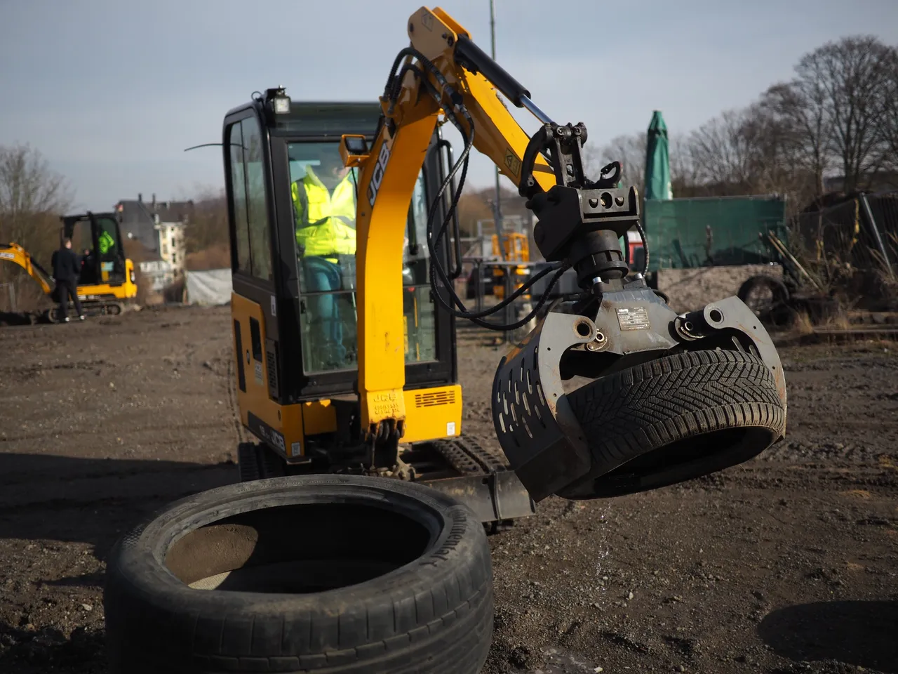 Person operating a mini excavator with a grapple to lift a tire