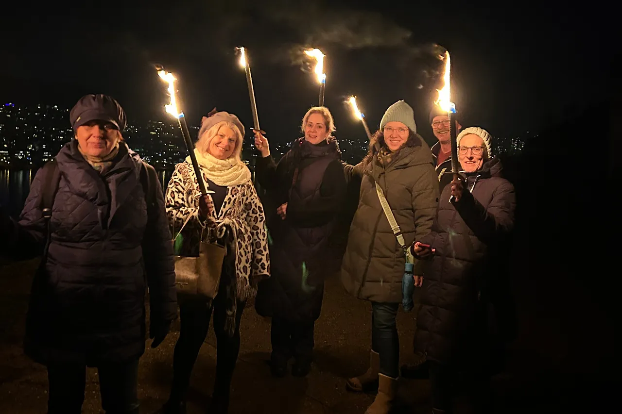 Group of friends holding burning torches on a winter evening walk above the lights of Rüdesheim am Rhein