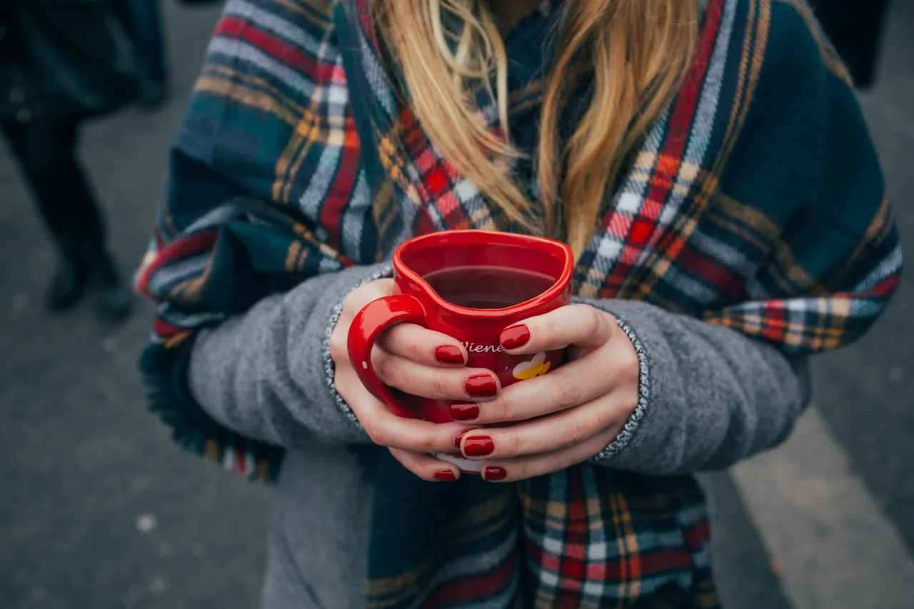 Woman in a woolly scarf warming her hands on a hot drink outdoors in winter