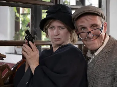 Two actors in vintage costumes posing with a revolver at a murder mystery dinner