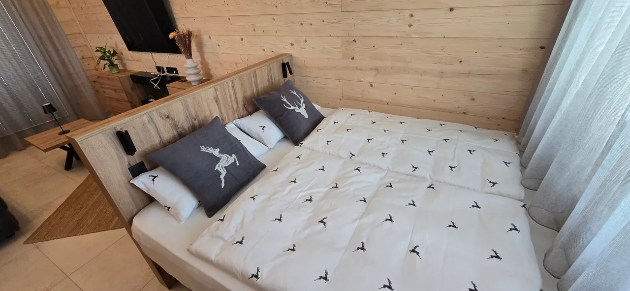 Chalet bedroom with double bed, deer-print bedding and grey deer cushions in a natural wood interior
