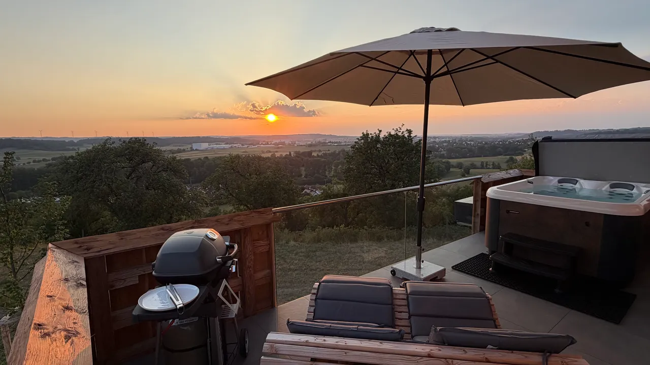 Private chalet terrace with hot tub, grill, loungers and parasol at sunset over the valley