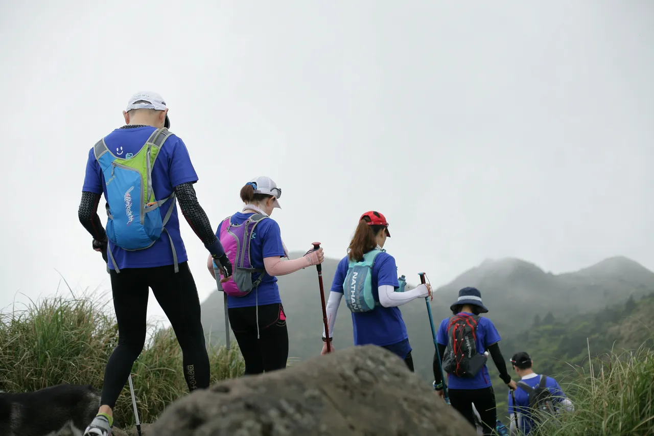 Group of hikers with walking poles trekking along a misty mountain ridge trail