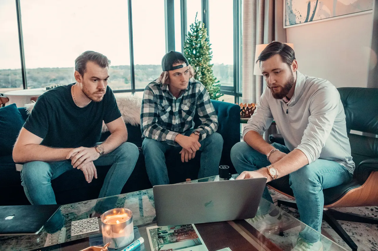 Three men sitting on a couch looking at a laptop