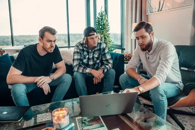 Three men sitting on a couch looking at a laptop