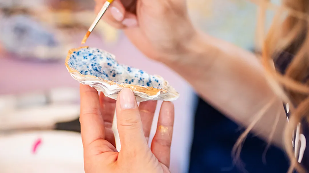 Hand painting a gold rim on a decorated oyster shell