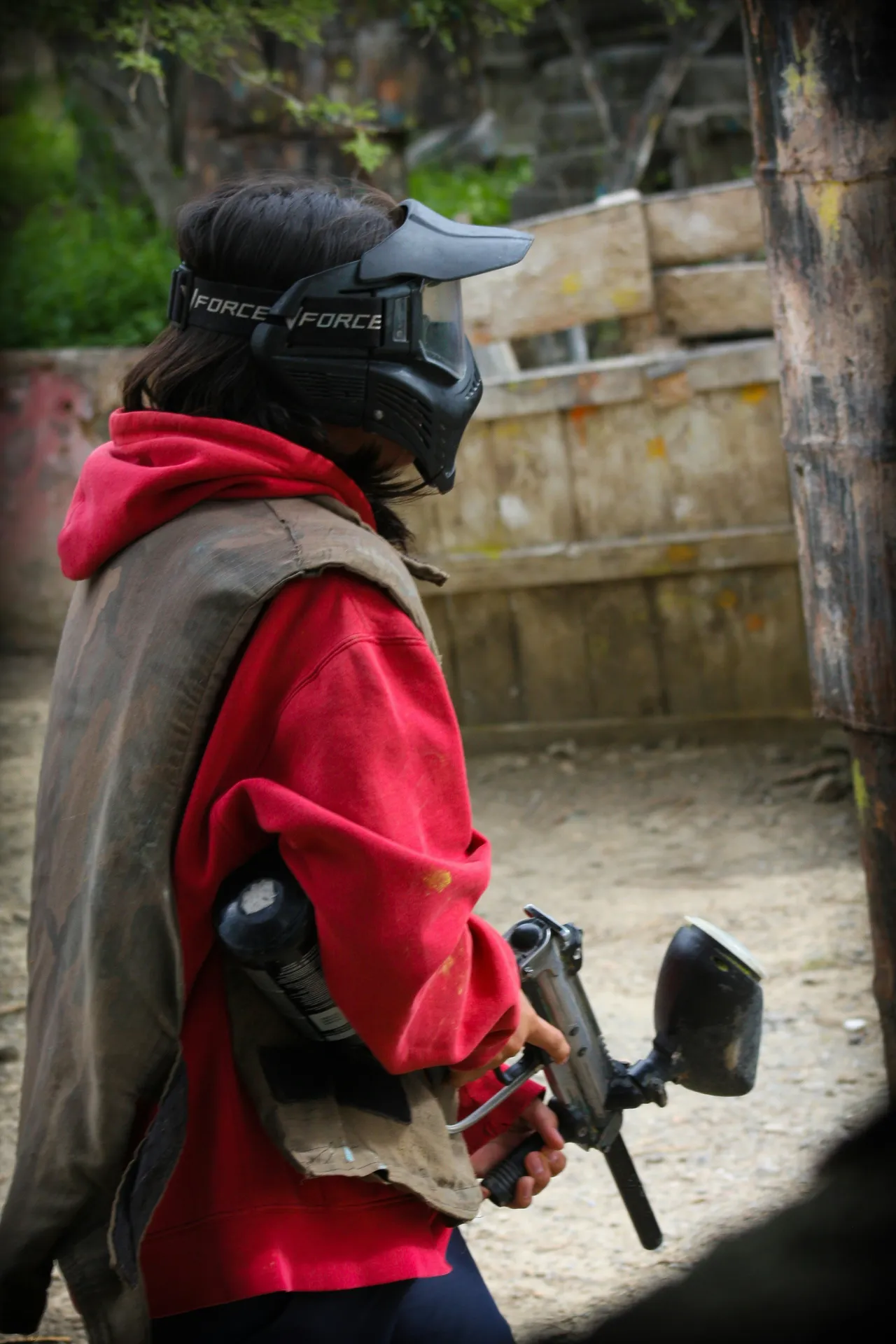 A paintball marker, protective safety goggles, and a camo jersey resting on a wooden bench.