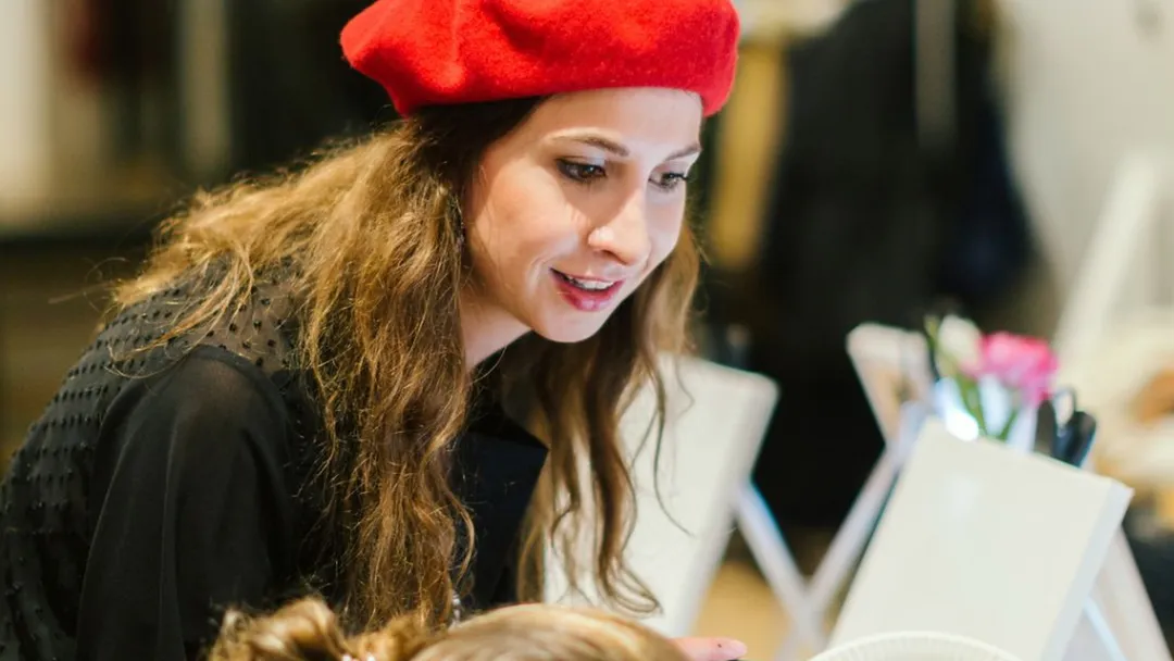 Painting instructor in a red beret guiding a participant with a palette of acrylic paints