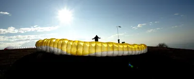 Yellow paraglider wing inflated on the ground against a bright sky
