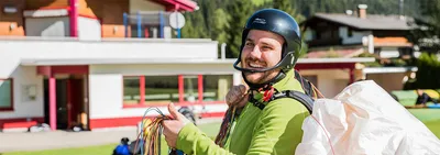 Smiling paragliding student wearing a helmet with his wing in the background