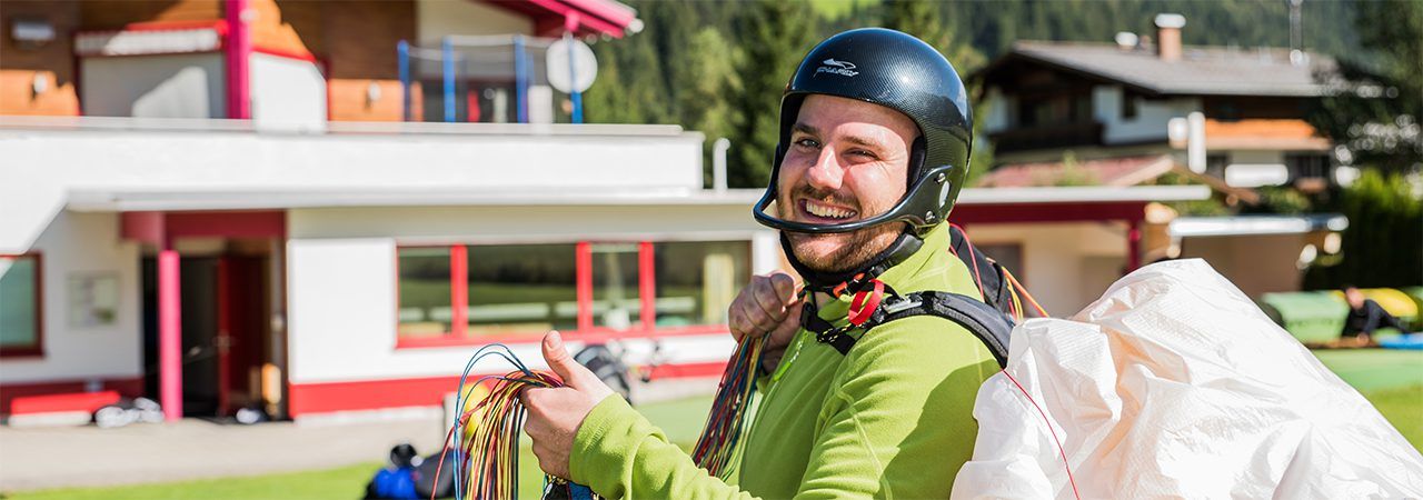 Smiling paragliding student wearing a helmet with his wing in the background