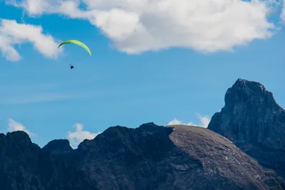 Paraglider flying high above a rocky mountain peak under a blue sky