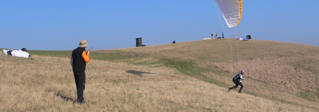 Paragliding students practising with their wings on a grassy training slope