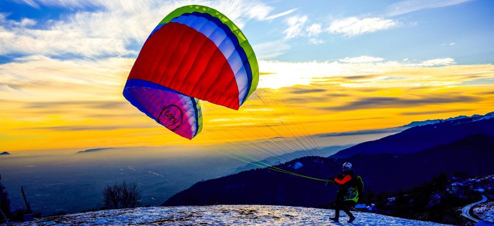 Pilot practising ground handling with a colourful paraglider at sunset