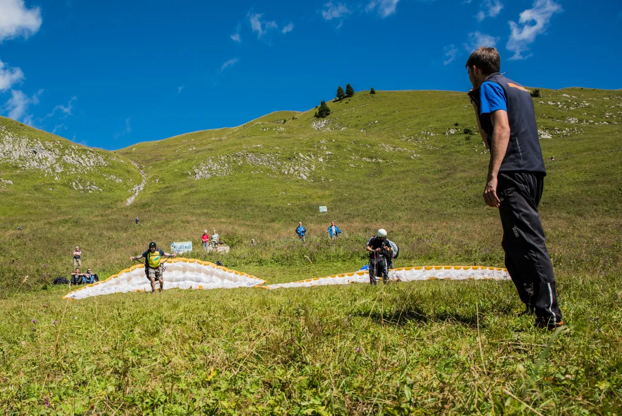 Paragliding instructor on a training slope with students and mountains in the background