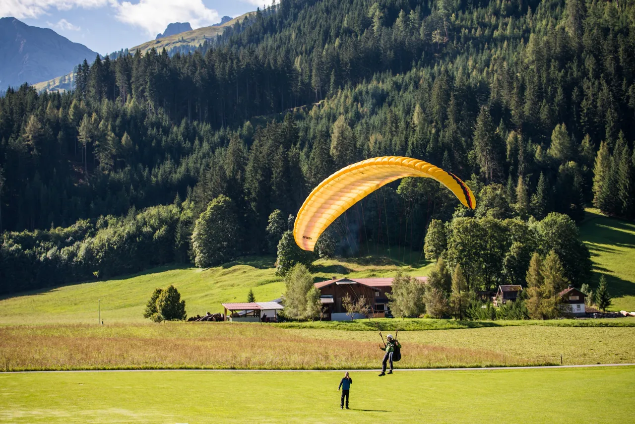Paraglider with yellow wing coming in to land in a green alpine valley