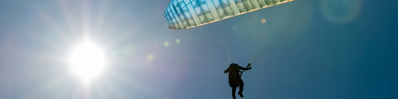 Paraglider flying in front of the sun against a blue sky