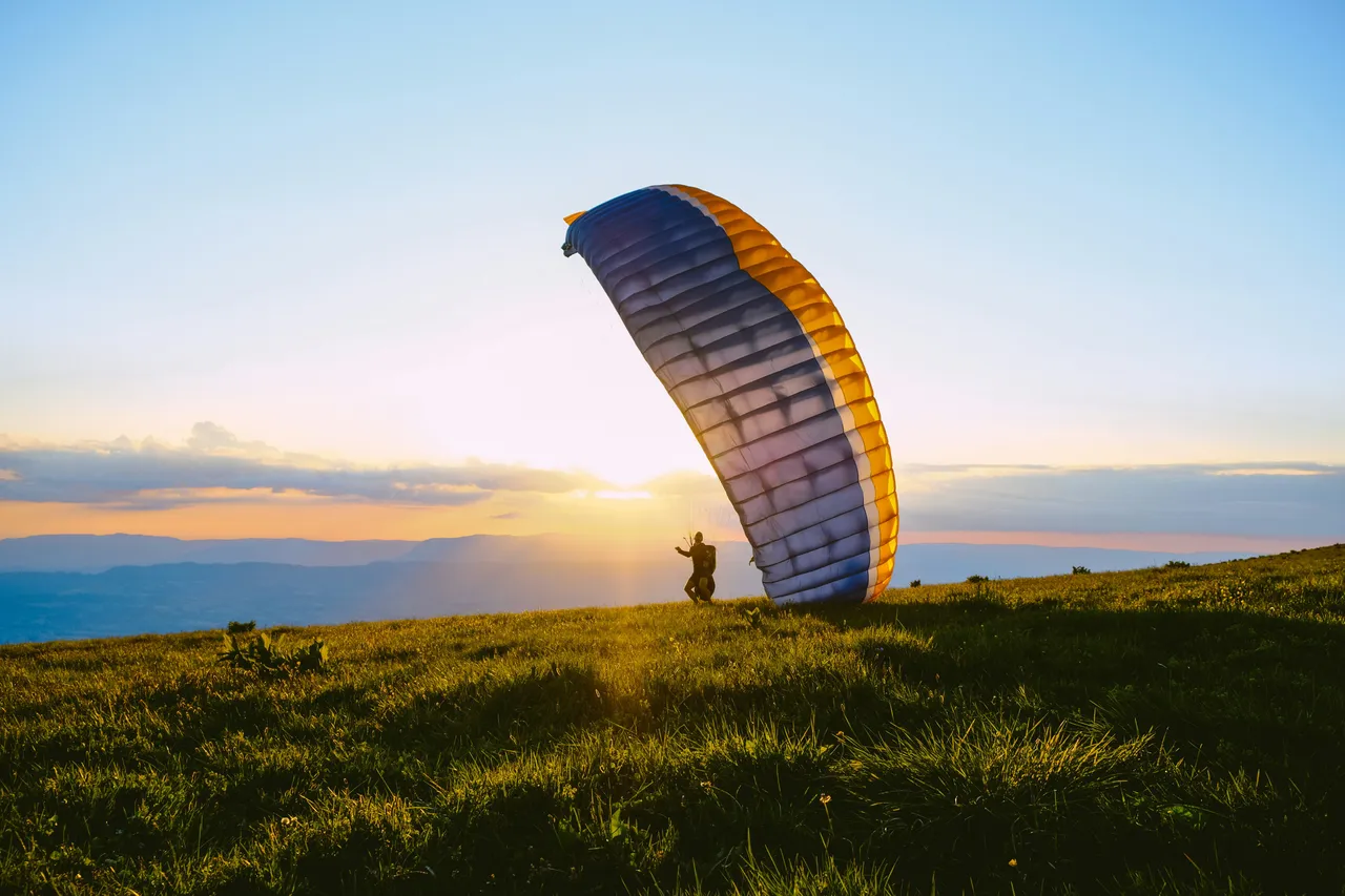 Person starting for a paragliding flight at sunset