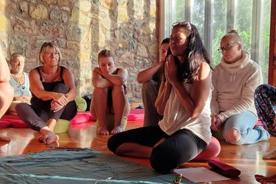 Participants sitting on cushions in a seminar room while a woman meditates with her hands pressed together