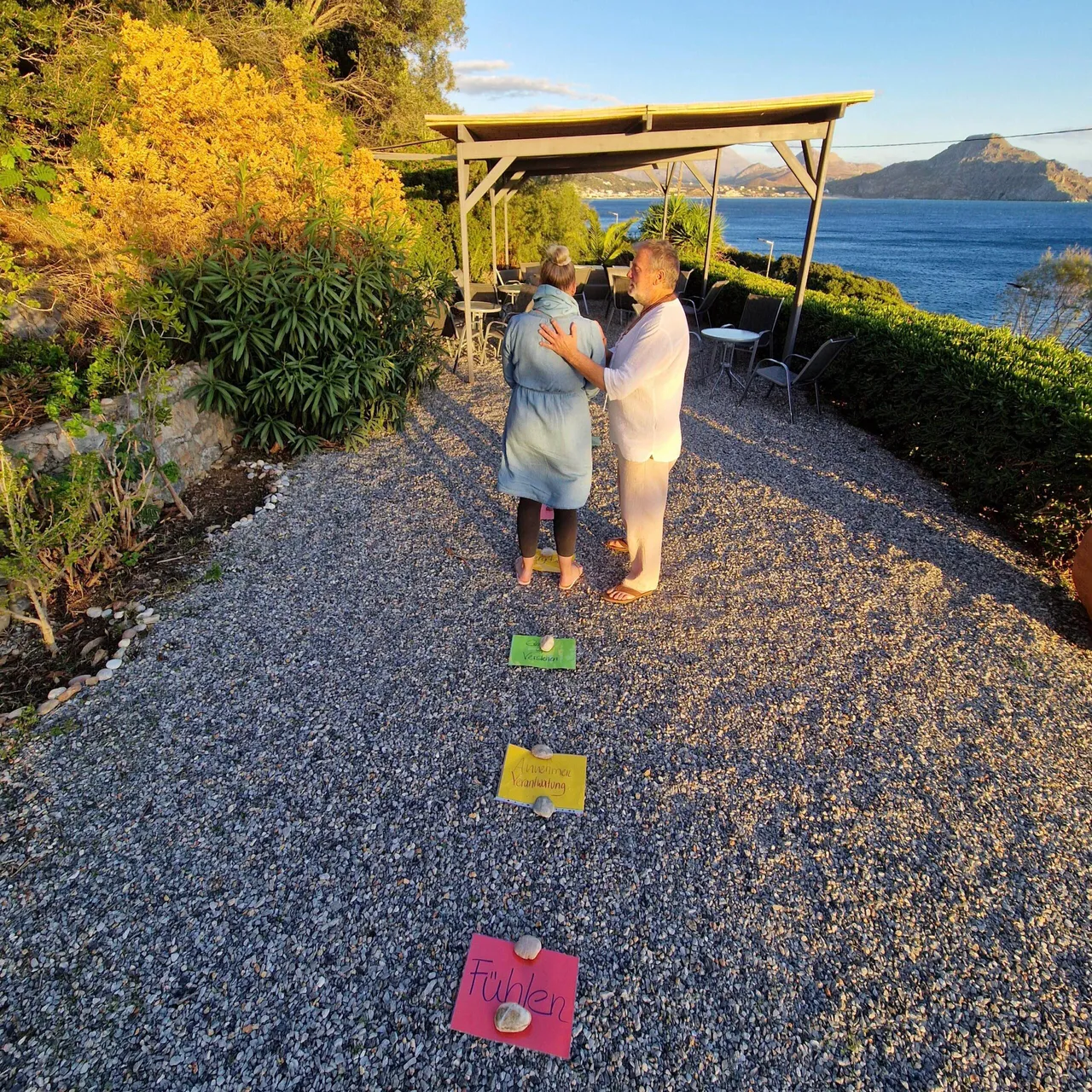 Seminar leader gently placing his hand on a participant’s back during a guided exercise on a garden terrace by the sea