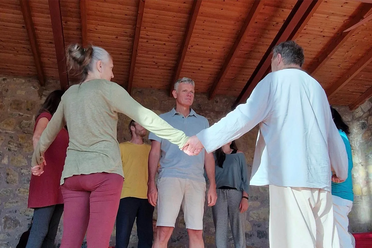 Participants standing in a circle and holding hands during a ritual under a wooden roof
