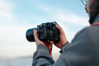 Man checking a mirrorless camera's screen while photographing outdoors against a blue sky