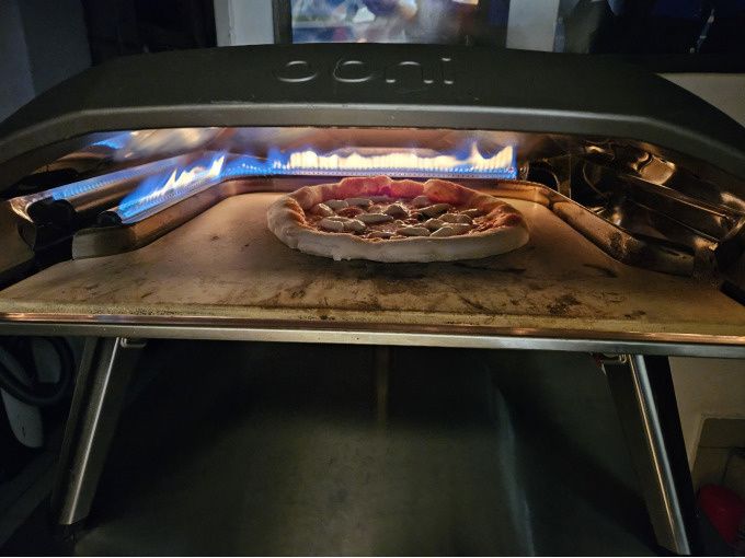 Pizza baking inside a gas-fired outdoor pizza oven with visible flames