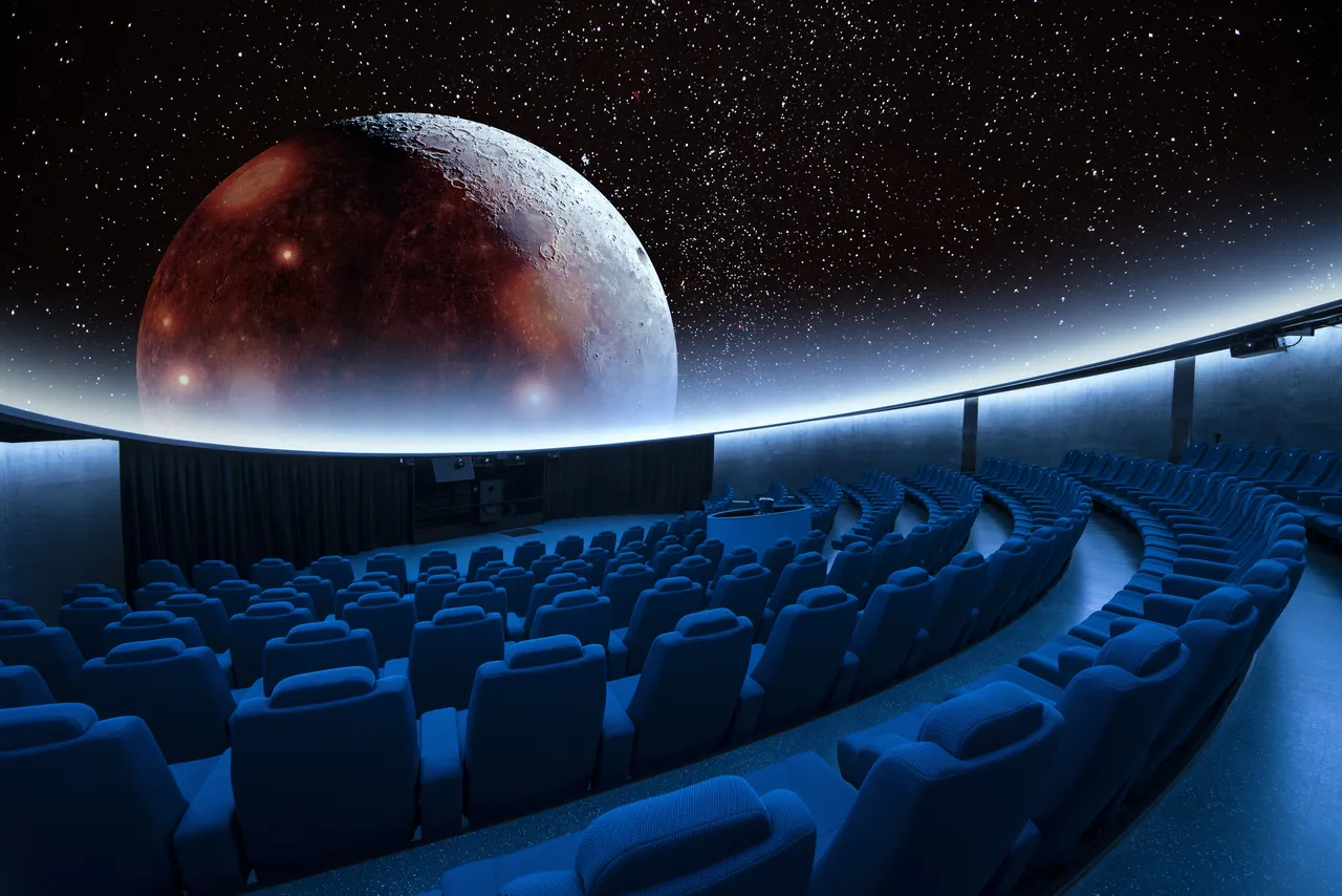 An empty planetarium dome theater featuring a massive, detailed projection of Mars or a reddish planet against a starry background.