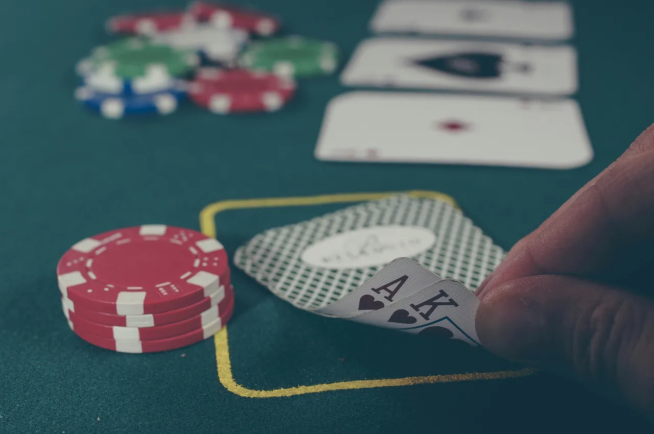 Hand holding an ace-king poker hand next to a stack of red chips on green felt