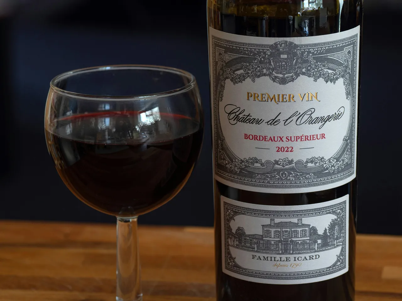 A bottle of a premium Bordeaux wine next to a glass filled with red wine