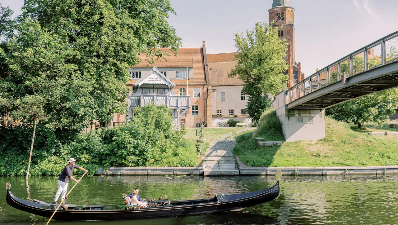 Gondolier steering a gondola along a green riverbank by the historic Dominsel in Brandenburg an der Havel