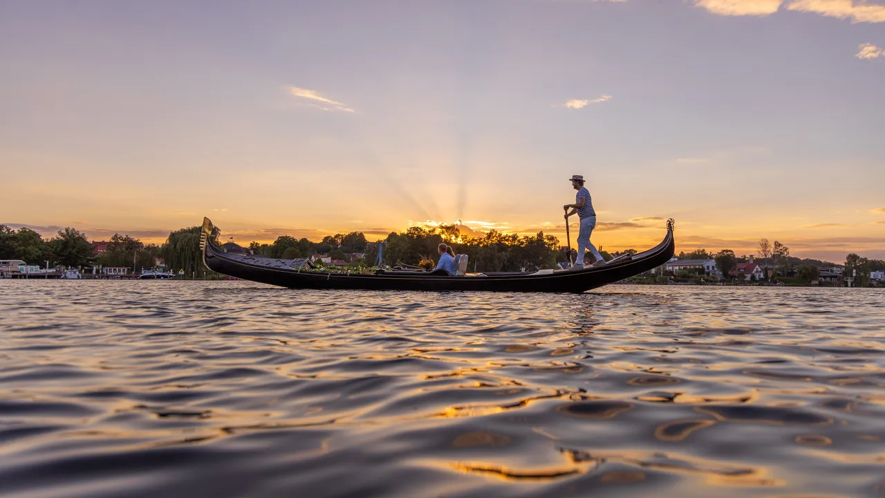 Gondolier rowing a traditional Venetian gondola across a calm lake at sunset
