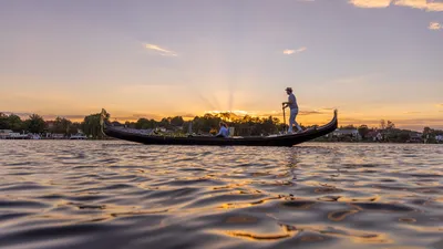 Gondolier rowing a traditional Venetian gondola across a calm lake at sunset