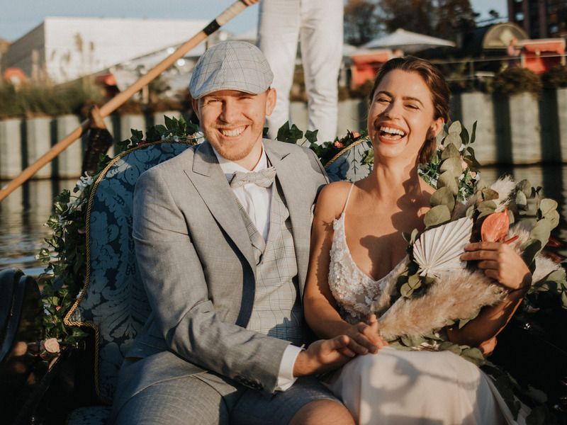Laughing bride and groom with a bouquet sitting together in a gondola