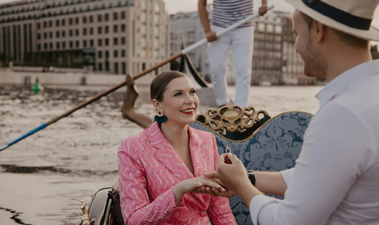 Woman in a pink suit smiling as her partner slips an engagement ring on her finger during a private gondola ride