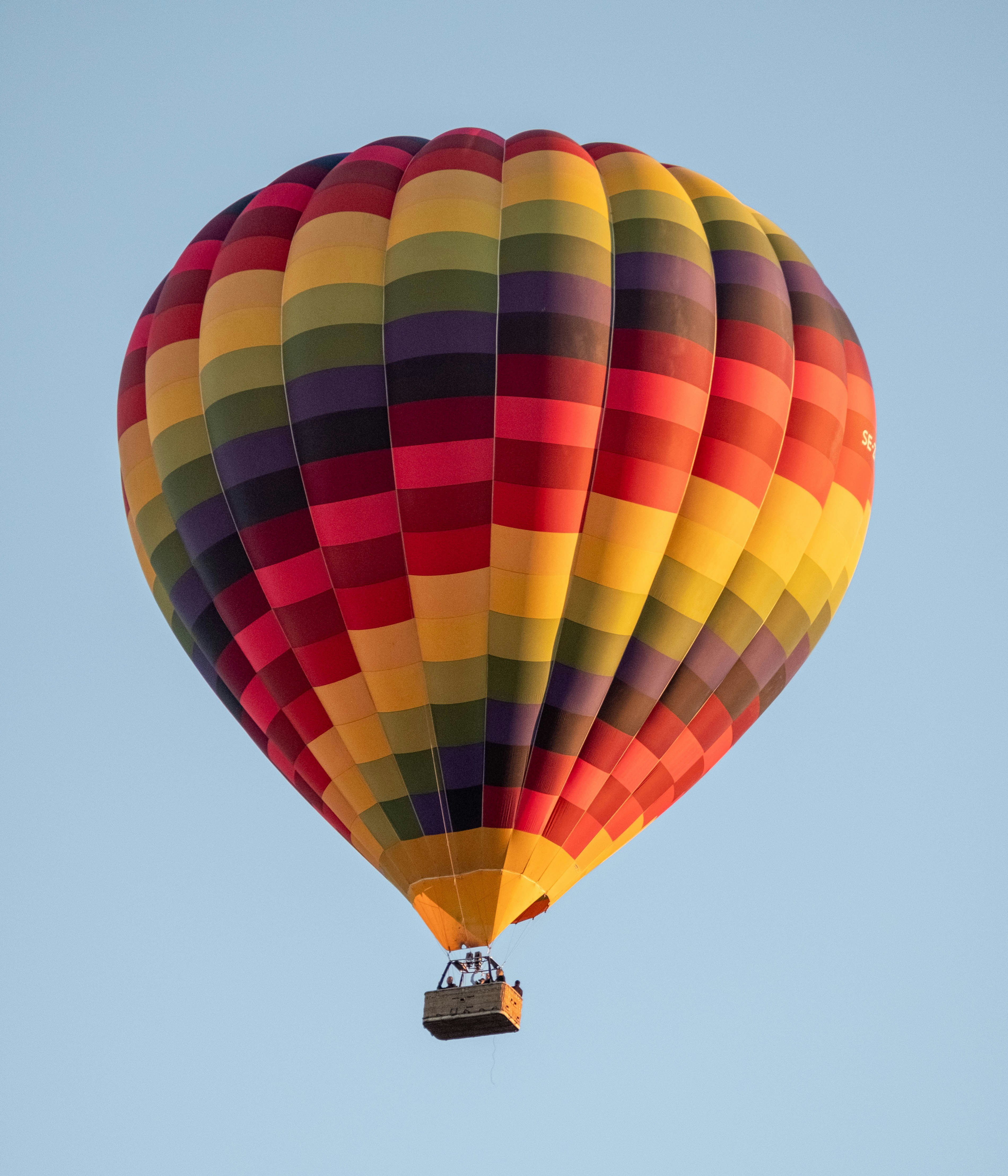 A colorful rainbow-patterned hot air balloon drifting in a clear, light blue sky.