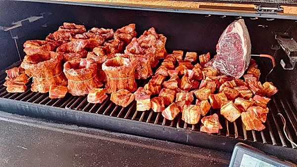 Raw seasoned pork rib crowns, meat cubes and a whole roast prepped on the smoker grate before cooking