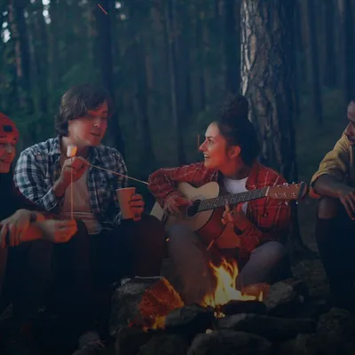Gifts for friends: group of friends playing guitar around a campfire in the forest
