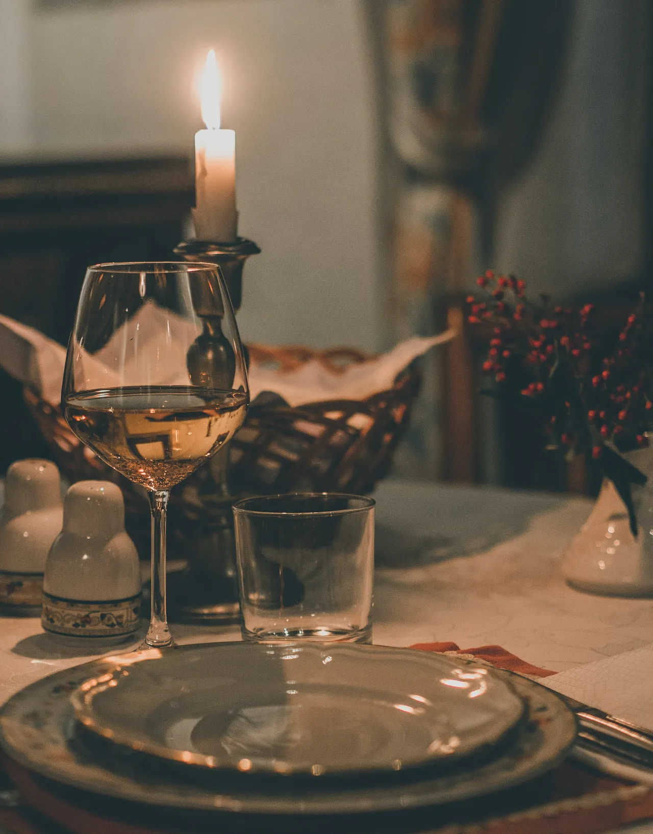 A beautifully arranged dinner table for two in a dimly lit room, illuminated by glowing candles, featuring wine glasses, plates, and upscale table settings.