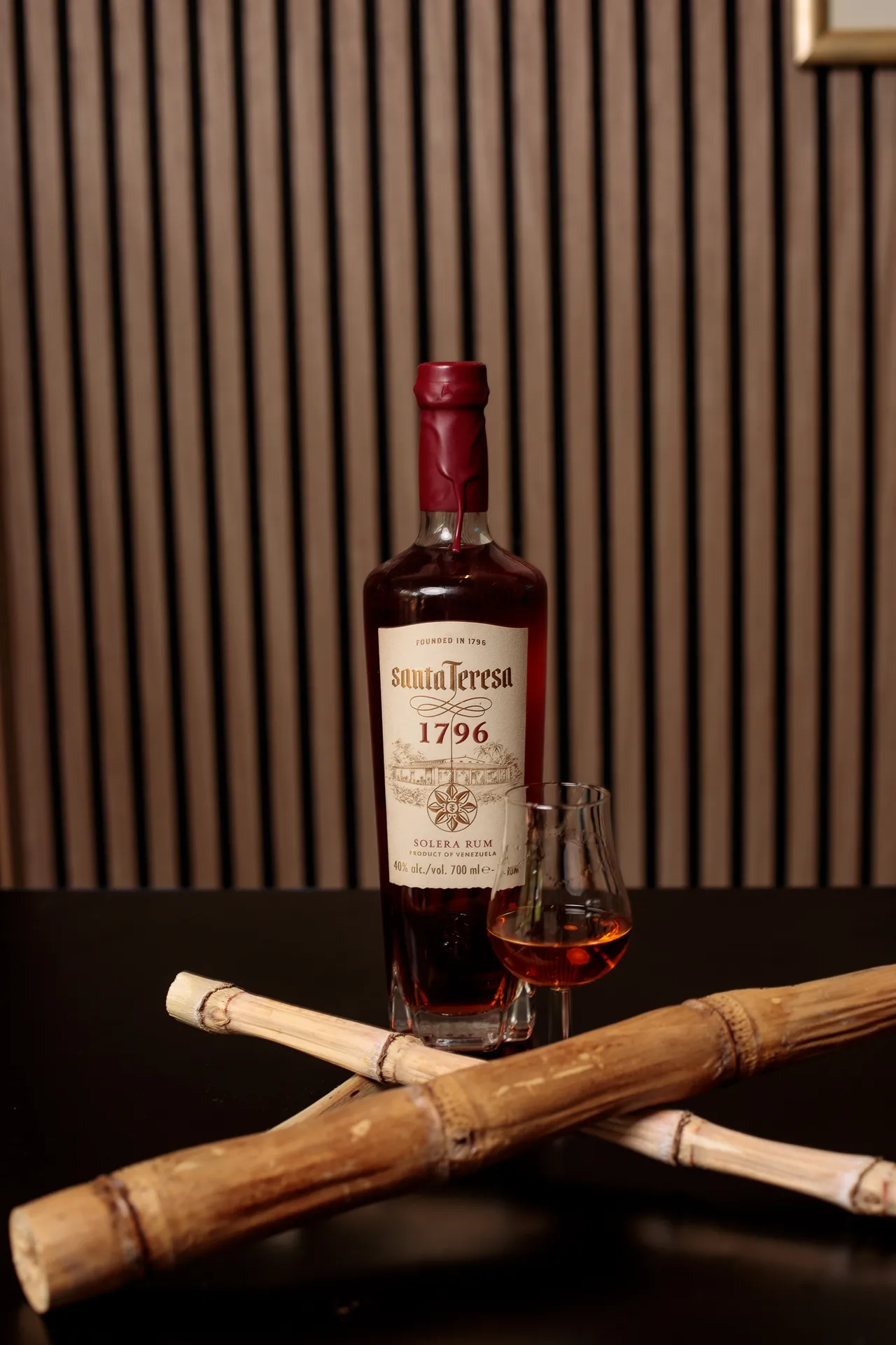 Bottle of Santa Teresa 1796 rum with a filled tasting glass, framed by crossed bamboo canes.