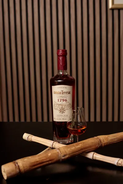 Bottle of Santa Teresa 1796 rum with a filled tasting glass, framed by crossed bamboo canes.