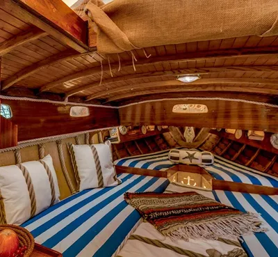 Wooden boat cabin with blue and white striped bunks, cushions and a woven blanket