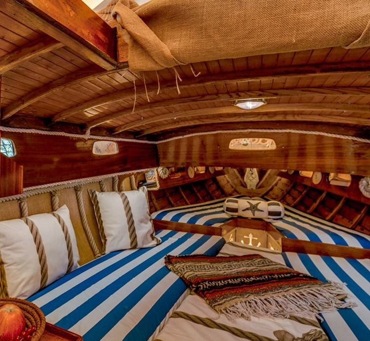 Wooden boat cabin with blue and white striped bunks, cushions and a woven blanket