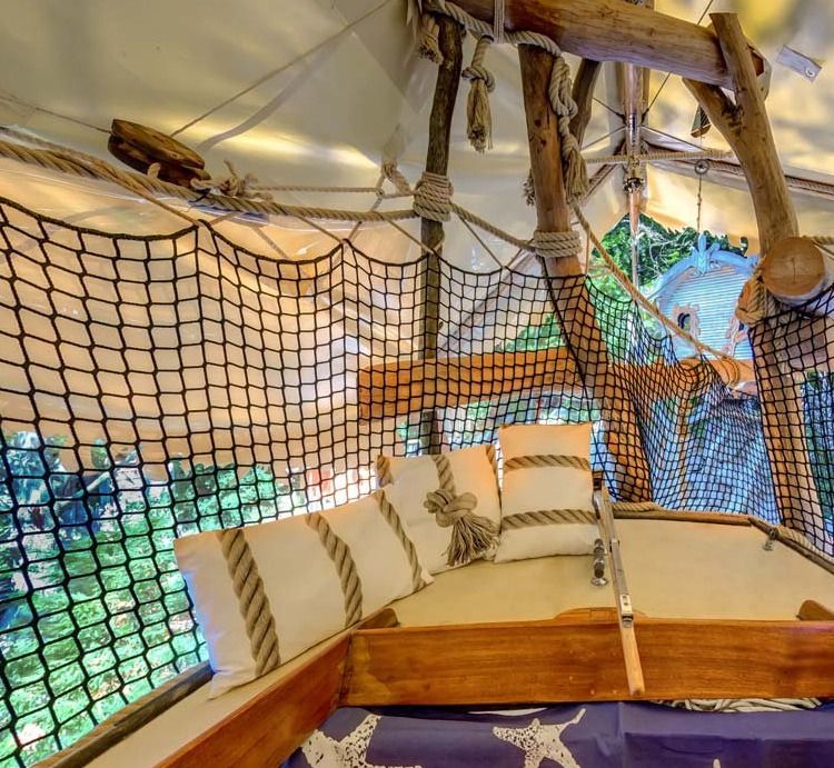 Lounge corner on a sailboat deck with cushions, wooden mast and rope safety net