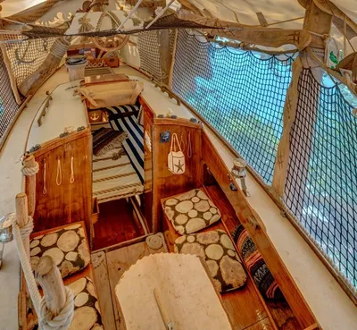 View down into a wooden sailboat treehouse with seat cushions, rope details and safety nets