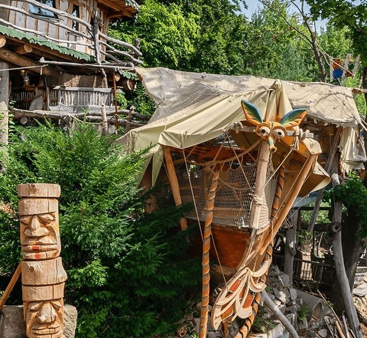 Sailboat treehouse on stilts among green trees with carved wooden totem figures