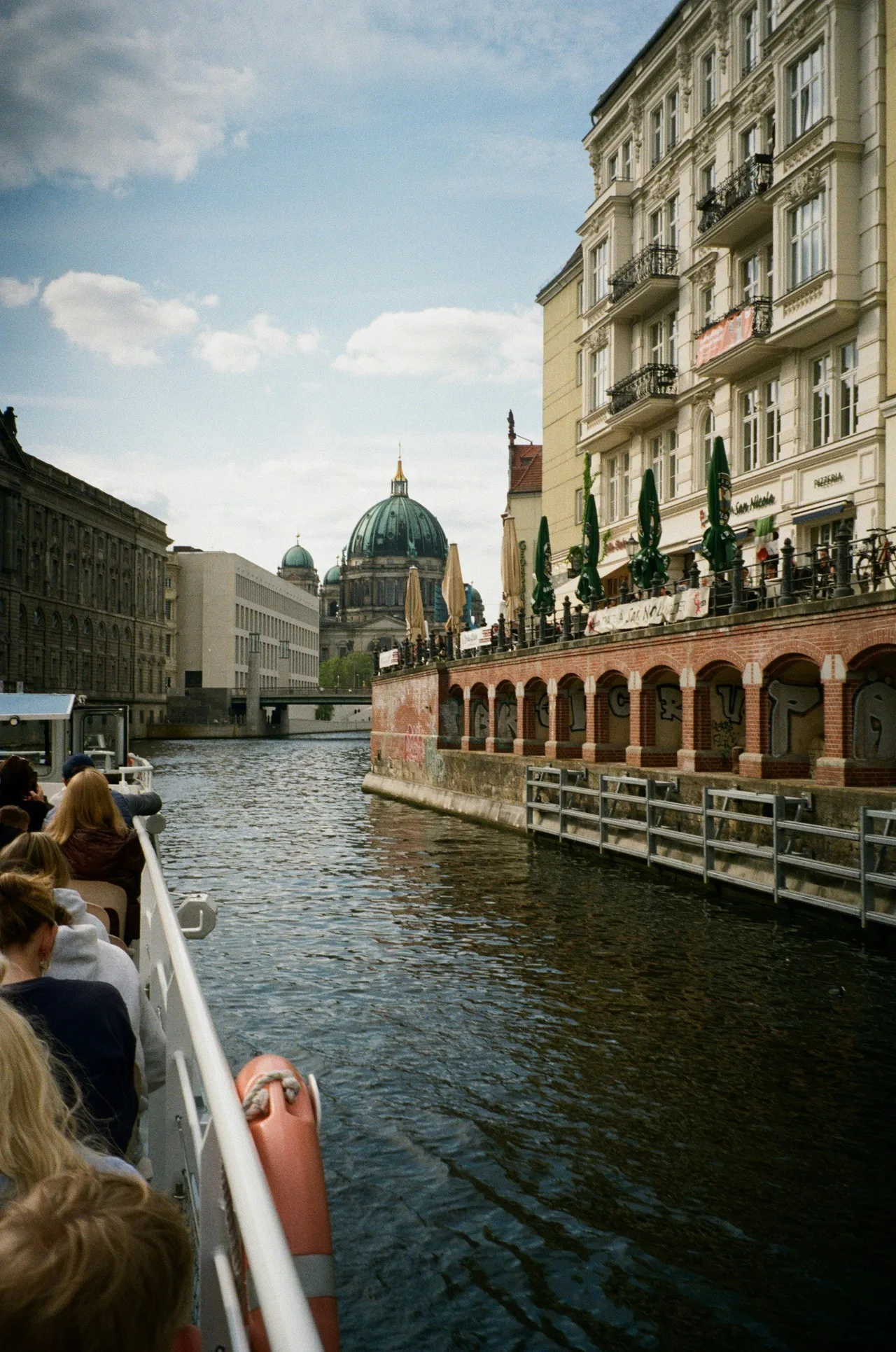 Passengers sitting on an open-top tour boat cruising down a calm river lined with trees.