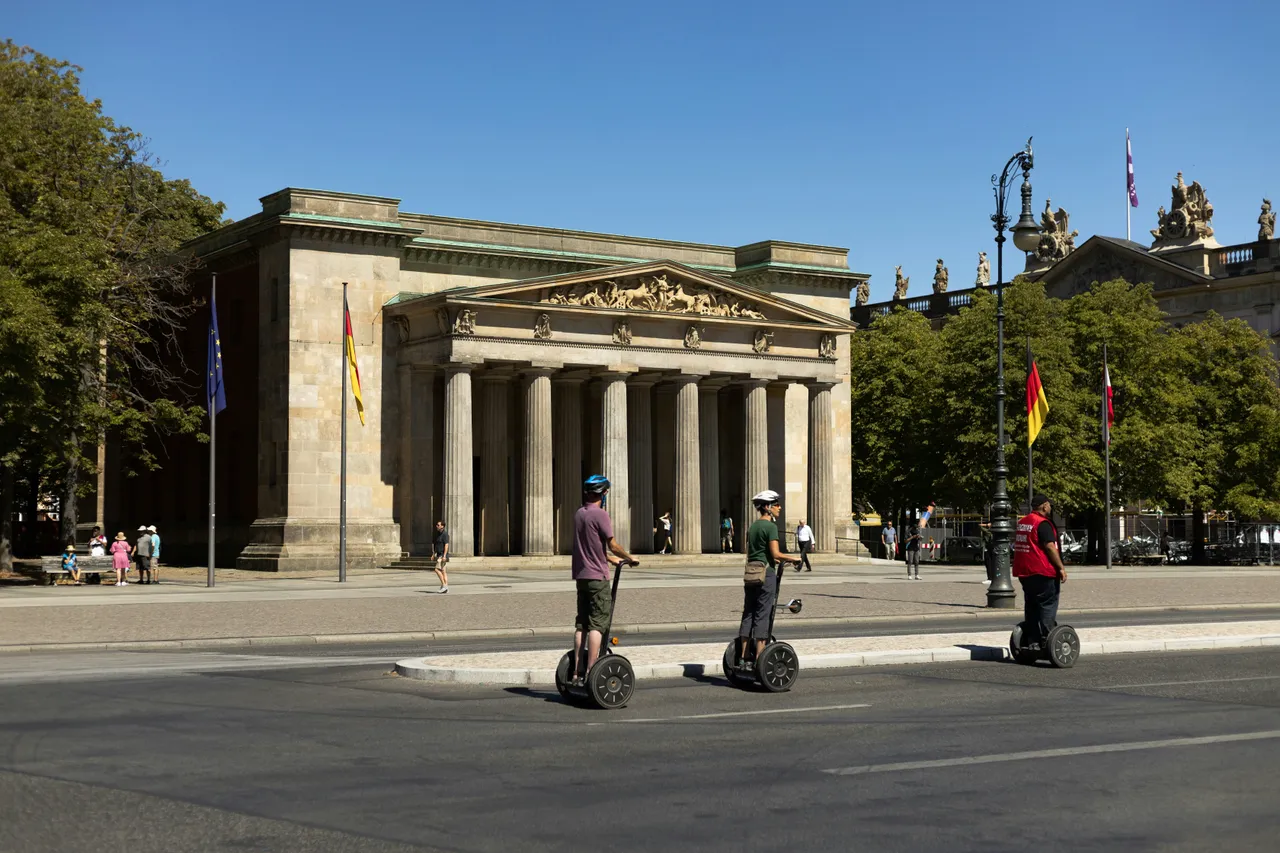 A small group of people riding Segways in a single-file line down a paved city street next to a brick building.