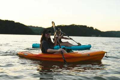 A person paddling a bright orange kayak through crystal-clear coastal waters.